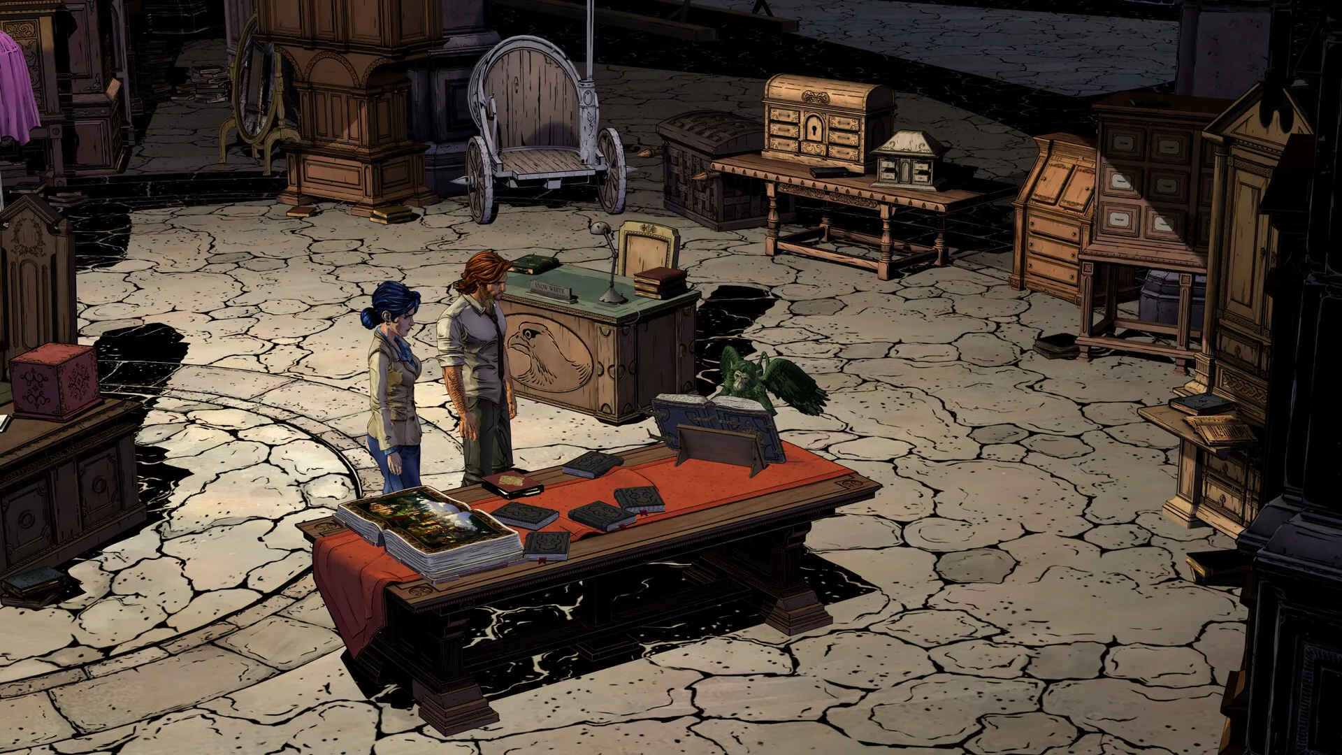 High-angle screenshot of a cracked stone floor in a dim room, with two small figures beside a red desk and stacked furniture around the walls.